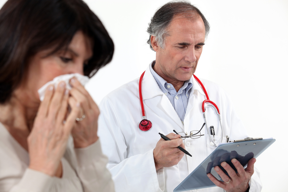 A woman blowing her nose at the doctor