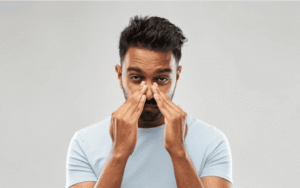 Man rubbing the bridge of his nose while experiencing sinus pressure and congestion after a cold.