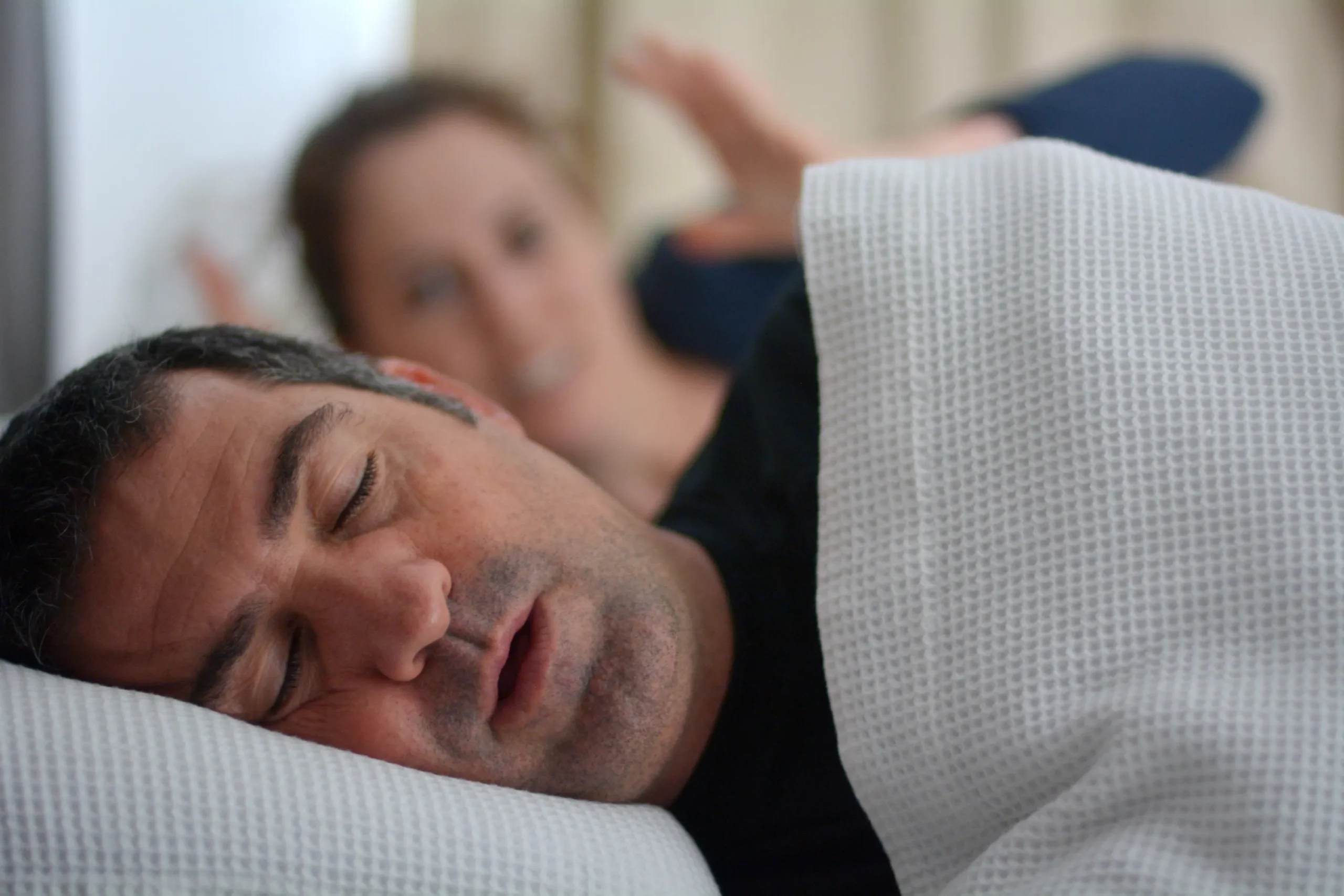 Man sleeping while his partner sits behind him